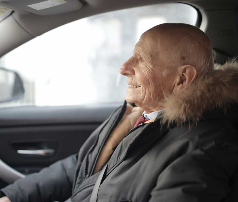 a smiling elderly man in the front seat of a car